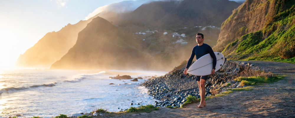 Man walking towards ocean carrying a surfboard