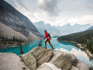 Traveller walking over rocks in front of mountains and lake